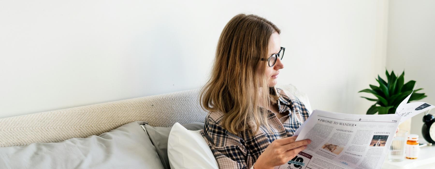 a woman reading a newspaper on a bed